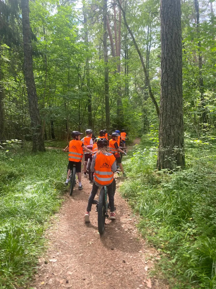Kinder mit orangefarbenen Aktivt-Uteliv-Westen fahren gemeinsam auf einem Waldweg